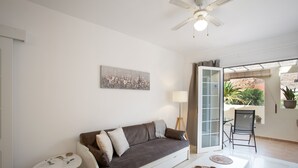 A modern living room with a sofa, a small table, a lamp, and a view through a glass door to an outdoor area.
