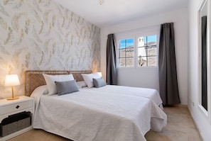 Une chambre avec un grand lit, une table de chevet, une lampe, une fenêtre avec des rideaux et une vue sur un paysage désertique.