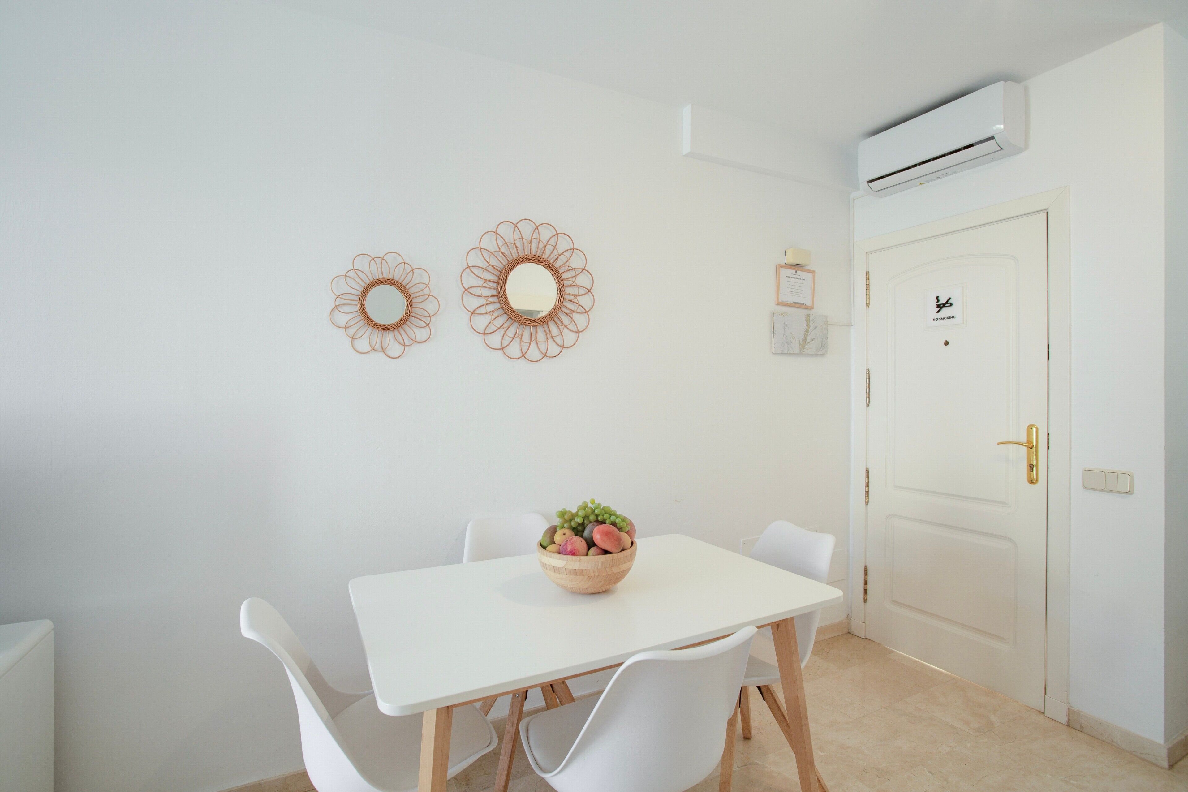 A white dining table with chairs, a fruit bowl, and two wall-mounted mirrors.