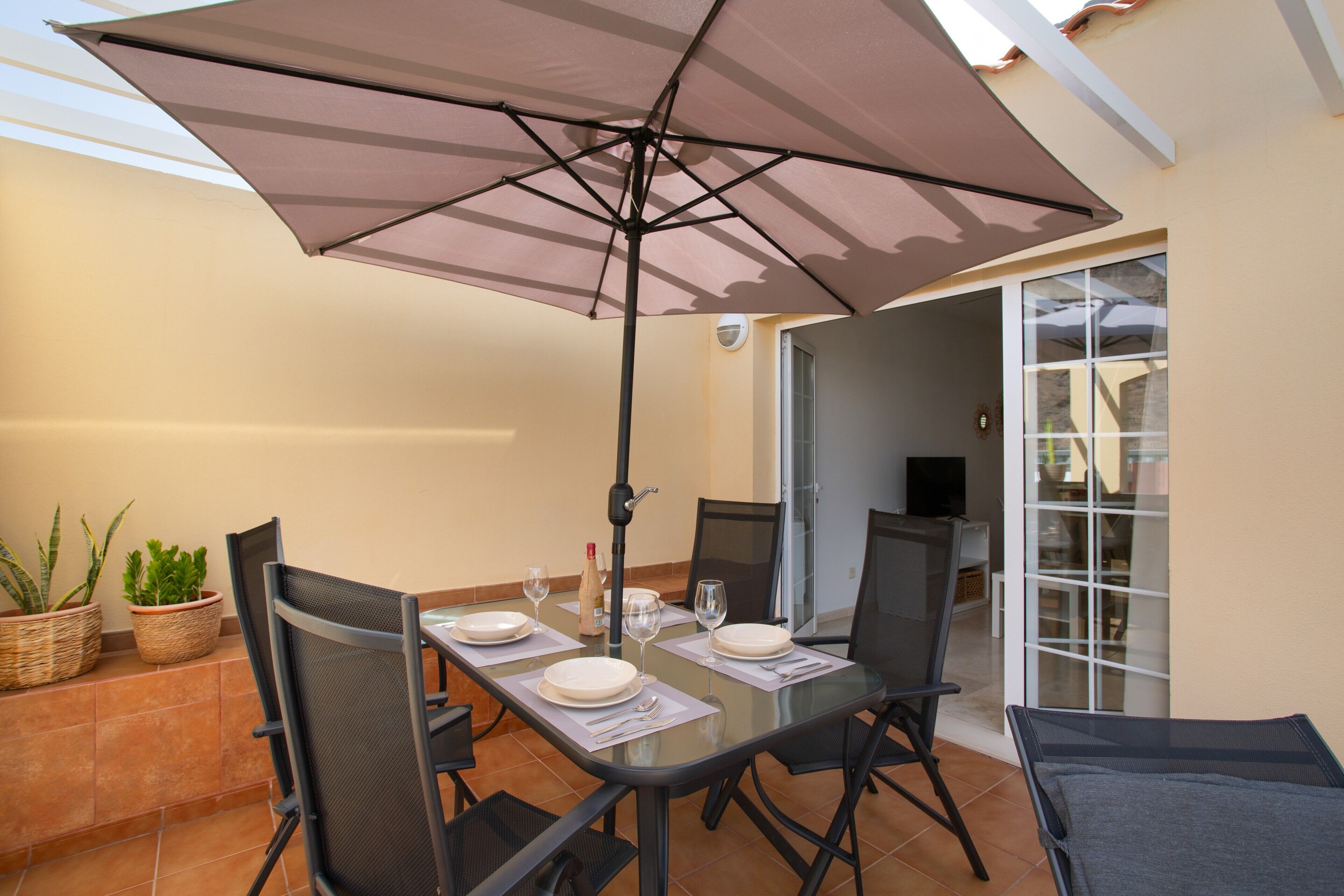 Un espace repas comprenant une table, des chaises, un parasol et des plantes en pot.