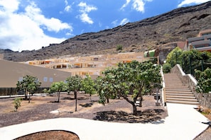 Une cour intérieure avec un escalier menant à un bâtiment, le tout entouré d’arbres et avec une chaîne de montagnes en arrière-plan.