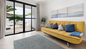 A modern living room with a yellow sofa, a grey rug, and a sliding glass door leading to an outdoor seating area. - Vacation Home "Puerto Hills" with Mountain View, Shared Pool & Wi-Fi (Puerto de la cruz)