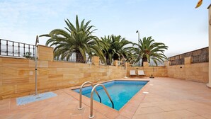 An outdoor swimming pool with a tiled deck, palm trees, and a stone wall. - Vacation Home "Puerto Hills" with Mountain View, Shared Pool & Wi-Fi (Puerto de la cruz)