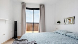 A bedroom with a bed, a window with curtains, a radiator, a small plant, and a framed picture on the wall. - Vacation Home "Puerto Hills" with Mountain View, Shared Pool & Wi-Fi (Puerto de la cruz)