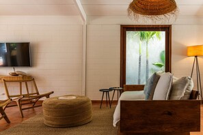 Une chambre avec un lit, une chaise, une petite table, un téléviseur et une fenêtre donnant sur des palmiers.
