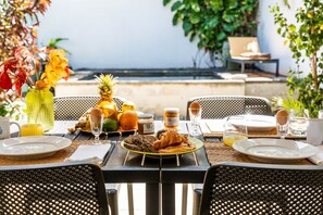 Area pranzo all'aperto con tavolo apparecchiato per la colazione, con croissant, frutta e bevande.