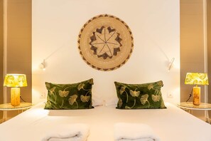 Un letto matrimoniale con due cuscini verdi, un elemento decorativo circolare fissato alla parete e due abat-jour.