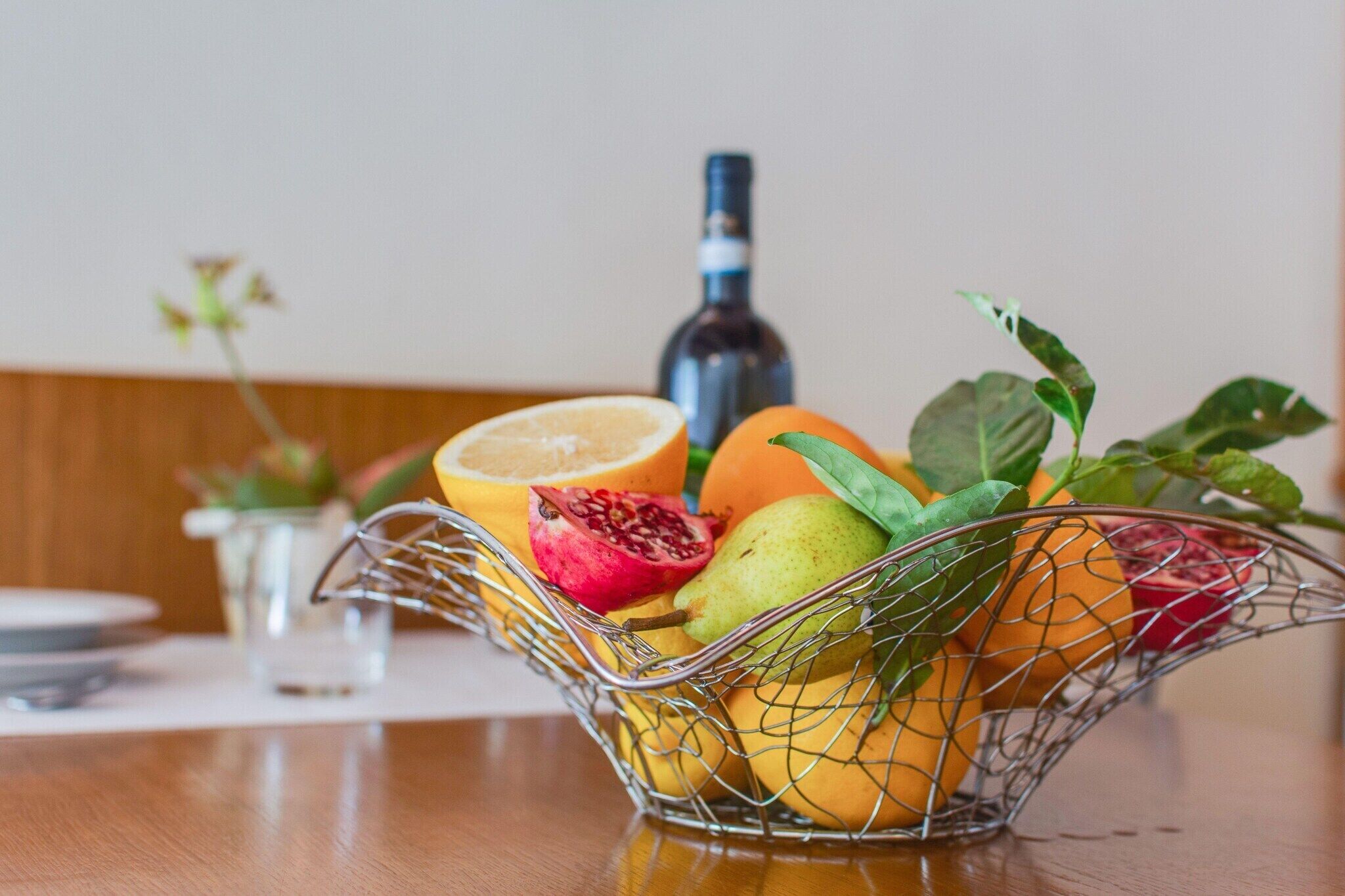 Una cesta de frutas sobre una mesa, con una botella al fondo.
