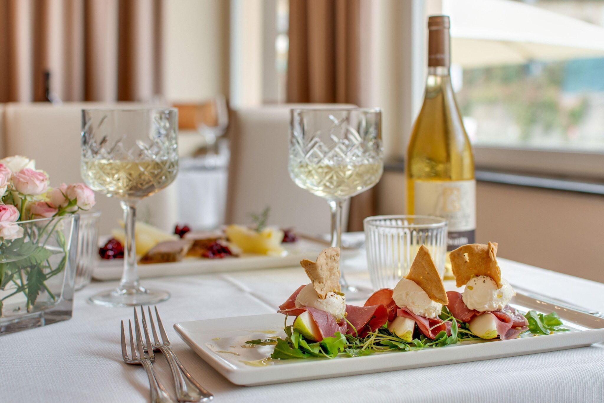 A dining table set with plates of food, wine glasses, and a bottle of wine.