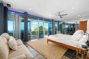 A spacious bedroom with a large bed, a sofa, and a TV. It features a sliding glass door leading to a balcony with a view of the ocean. - Breathtaking Oceanfront Studio with Hot Tub | Sunset Cliffs (San Diego)