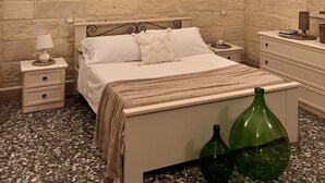 A bedroom with a stone wall, a bed with white bedding, a nightstand with a lamp, and a dresser with a mirror. - Typical Salento romantic suite (Borgagne)