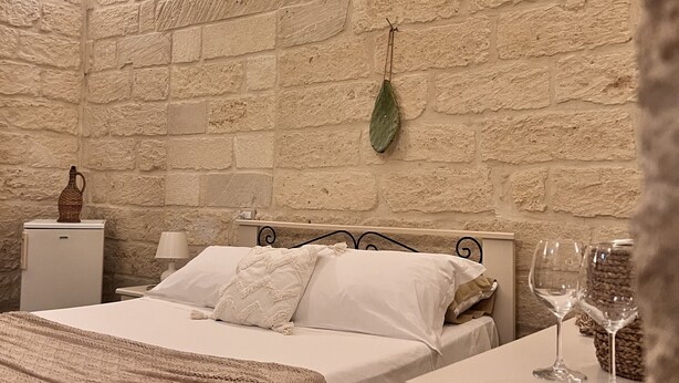 A bedroom with a brick wall, a bed with white linens, a bedside table with a lamp, and a small table with two wine glasses. - Typical Salento romantic suite (Borgagne)