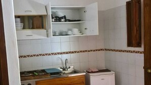 A compact kitchen with a stove, sink, and a small refrigerator. There are cabinets above the counter and a tiled backsplash.