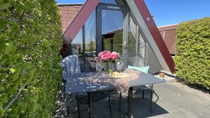 A modern outdoor dining area with a table and chairs, a glass door, and a view of the garden. - Hotelhuisjes Andijk (Andijk)