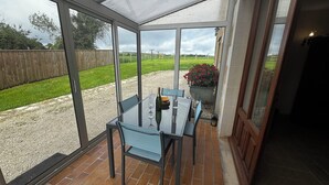 A conservatory with a glass table and chairs, a potted plant, and a view of a grassy yard.