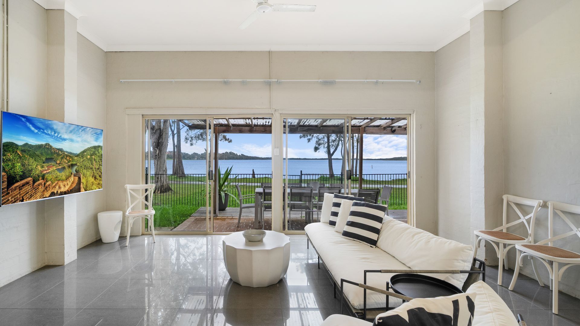 A modern living room with a large sliding glass door leading to a balcony with a view of a lake.
