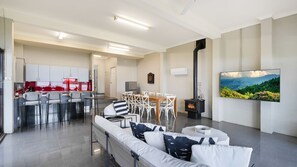 A modern living room with a sofa, chairs, a dining table, a TV, and a fireplace.