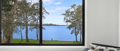 Una habitación con un amplio ventanal con vistas a un lago, rodeada de árboles.