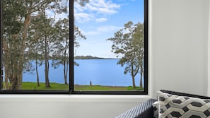 A room with a large window overlooking a lake, surrounded by trees. - Stillwater Lakehouse - Waterfront with Spa (Buff Point)