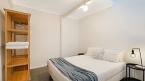 A bedroom with a bed, a wooden wardrobe, a bedside table with a lamp, and a ceiling light.