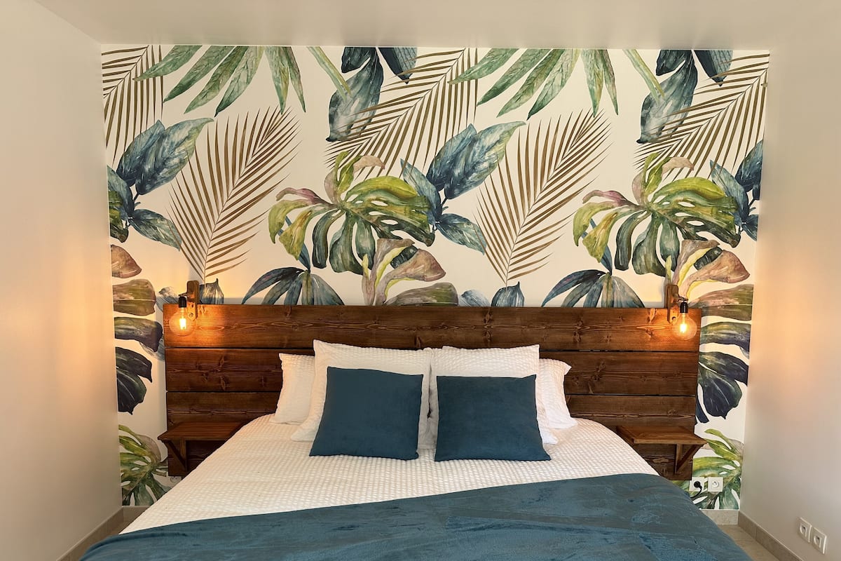 A bedroom with a wooden headboard, a white textured bedspread, two dark pillows, and a blue blanket.