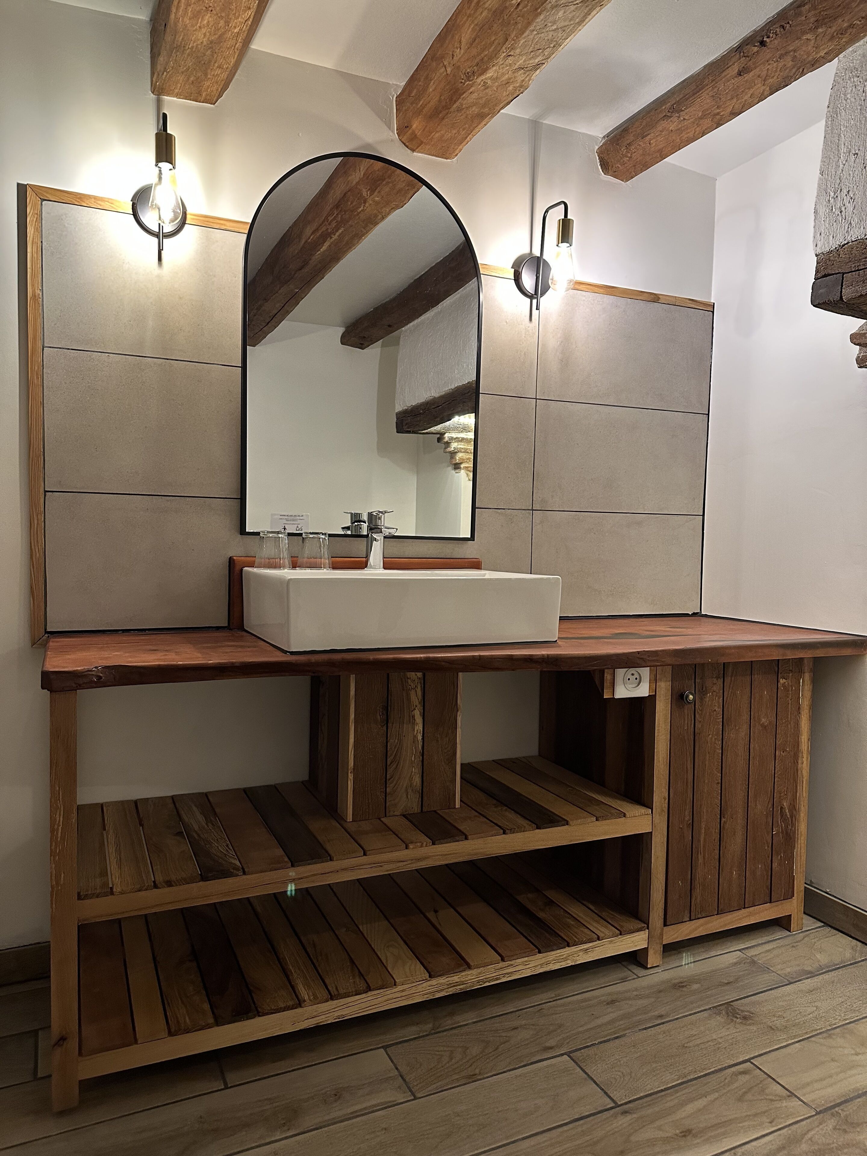 A bathroom with a wooden vanity, a large mirror, and two wall-mounted light fixtures.