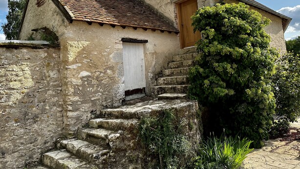 A rustic stone building with a wooden door, a chimney, and a small staircase leading to the entrance. - Domaine de Couilleuse (Saint-Laurent-Nouan)