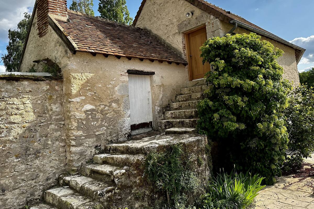 A rustic stone building with a wooden door, a chimney, and a small staircase leading to the entrance.