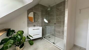 Une salle de bain moderne avec une douche en verre, un meuble-lavabo blanc et une grande plante en pot.