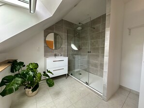 Un bagno moderno con cabina doccia in vetro, mobile lavabo bianco e un'ampia pianta in vaso.