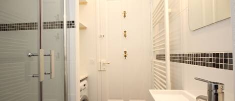 A bathroom with a glass shower enclosure, a white door, a washing machine, and a sink with a chrome faucet.
