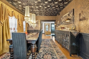 Ein Essbereich mit Holztisch, Stühlen und einer Chandelier. Es gibt eine Bar mit einer Theke und Hockern. Der Raum hat einen Wand mit Muster und eine Ziereindecke.