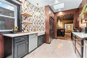 A modern kitchen with a herringbone patterned backsplash, dark cabinetry, and a window providing natural light. - The Gatsby - Gorgeous Midtown Stunner (sleeps 8) (Kansas City)