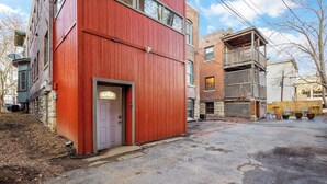 Un immeuble à plusieurs étages, doté d’une façade rouge, d’une porte d’entrée bien visible et d’un espace de stationnement agrémenté de plantes en pot.