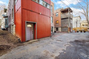 A multi-story building with a red facade, a visible entrance door, and a parking area with potted plants. - The Gatsby - Gorgeous Midtown Stunner (sleeps 8) (Kansas City)