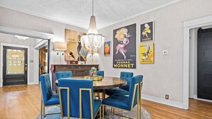Un coin repas avec une table ronde, des chaises à revêtement bleu, un lustre et des œuvres d’art murales.