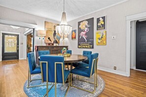 A dining area with a round table, blue upholstered chairs, a chandelier, and wall art. - The Gatsby - Gorgeous Midtown Stunner (sleeps 8) (Kansas City)