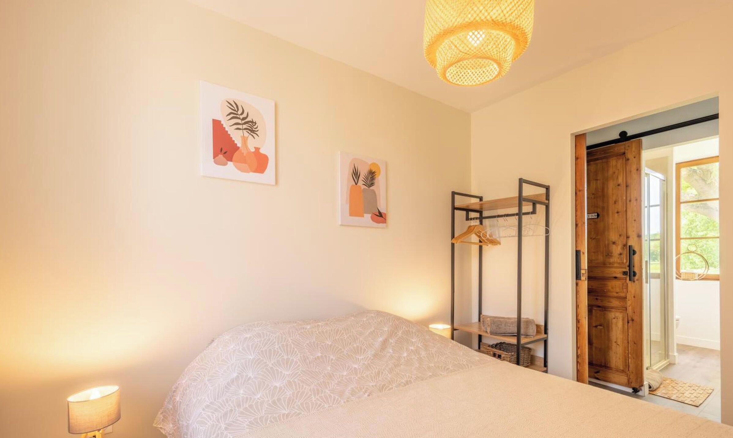 A bedroom with a bed, a hanging clothes rack, and two wall-mounted artworks.