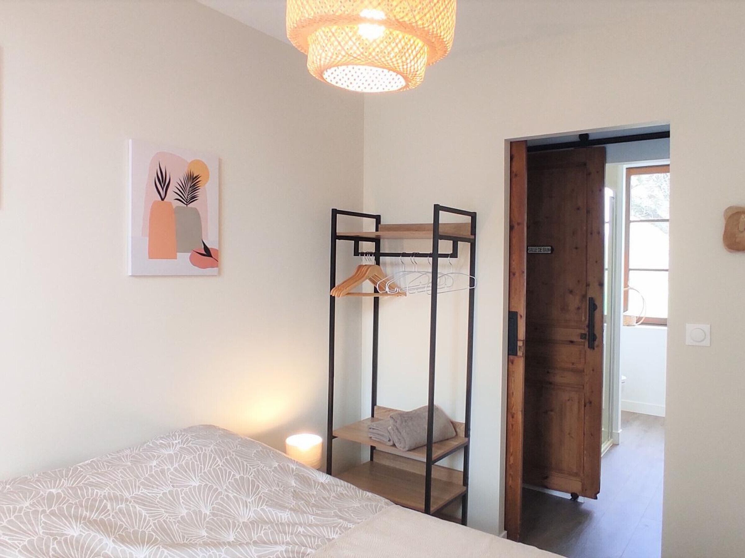 A bedroom with a bed, a hanging clothes rack, a door, and a wall-mounted artwork.