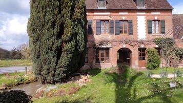 A traditional brick house with a large coniferous tree, a stone pathway, and a small stream.