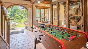 Una habitación con mesa de fútbol, vigas de madera y ventanas amplias.