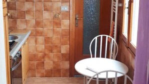 A compact kitchen with a tiled backsplash, a wooden door, and a small dining area with a white chair. - Bright apartment by the sea (Grimaldi)