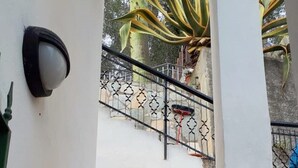A narrow staircase with white walls and a metal railing, leading to a courtyard with a palm tree and a stone wall. - Bright apartment by the sea (Grimaldi)