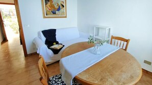 A room with a white sofa, a wooden dining table with a placemat, a small white side table, and a painting on the wall. - Bright apartment by the sea (Grimaldi)