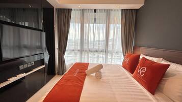 A hotel room with a large bed, a flat-screen TV, and a view of the city through sheer curtains.