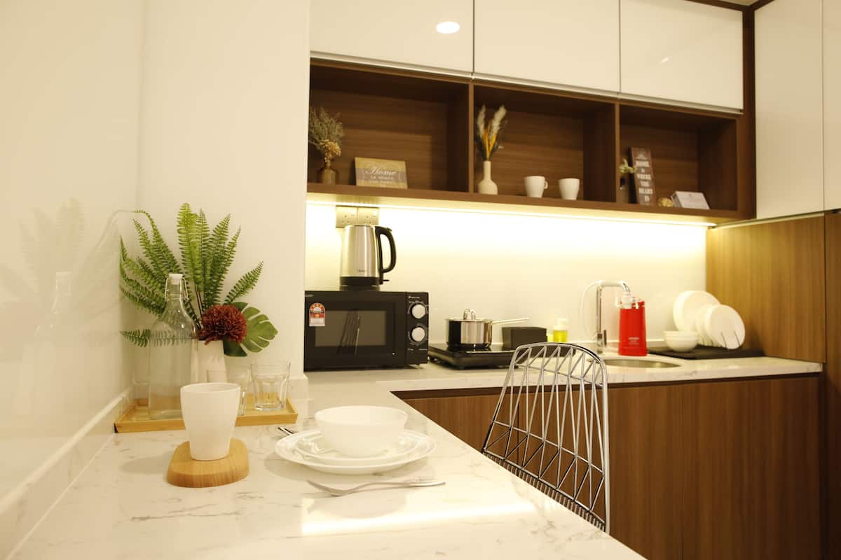 A modern kitchen with a marble countertop, a microwave, a kettle, and a sink.