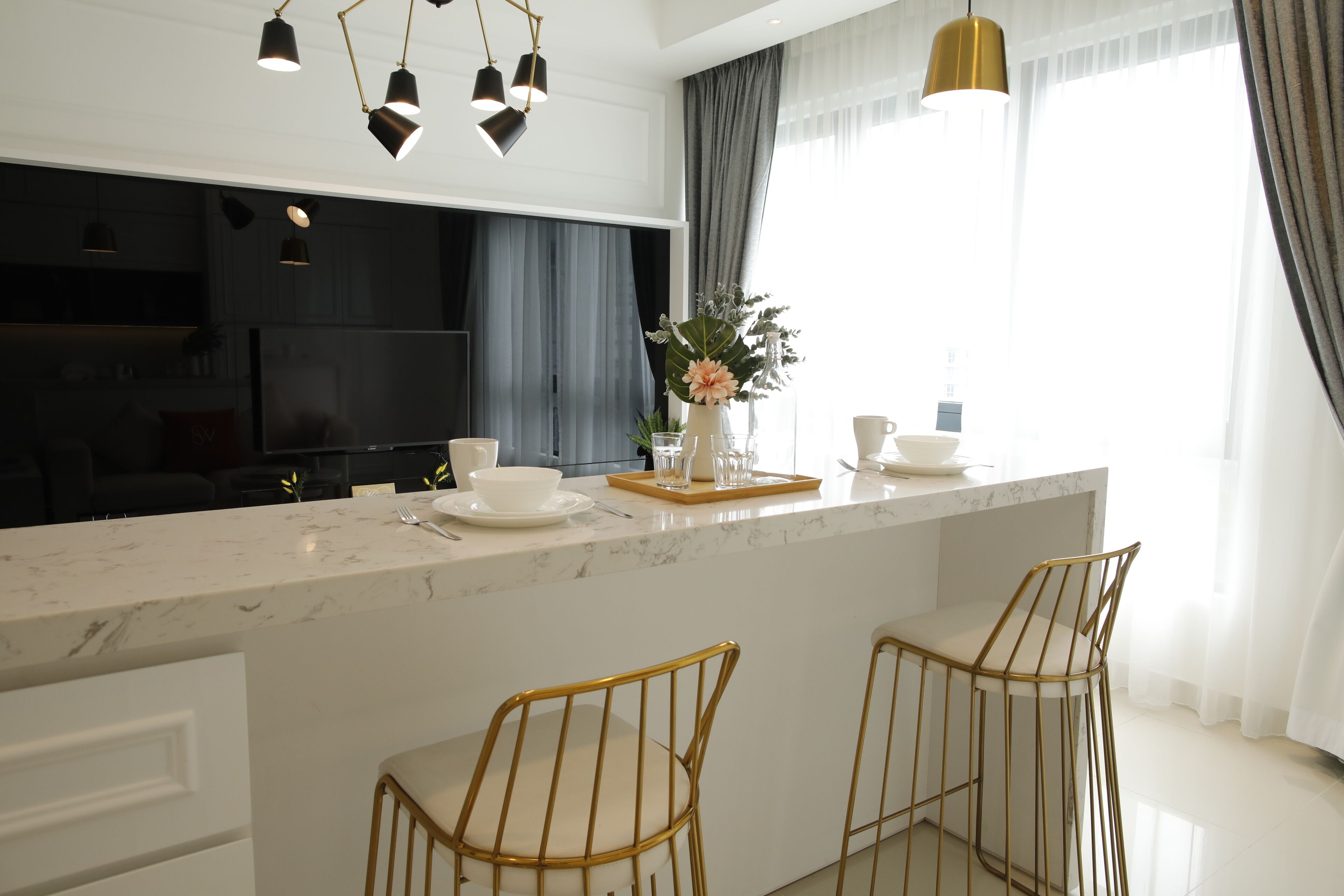 A modern kitchen with a marble countertop, two gold chairs, and pendant lighting.