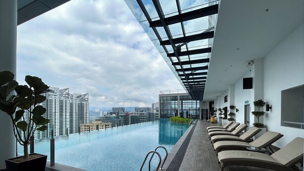 A modern indoor pool with a glass ceiling, lounge chairs, and a view of the cityscape. - NOVO Serviced Suites by Widebed (Kuala Lumpur)