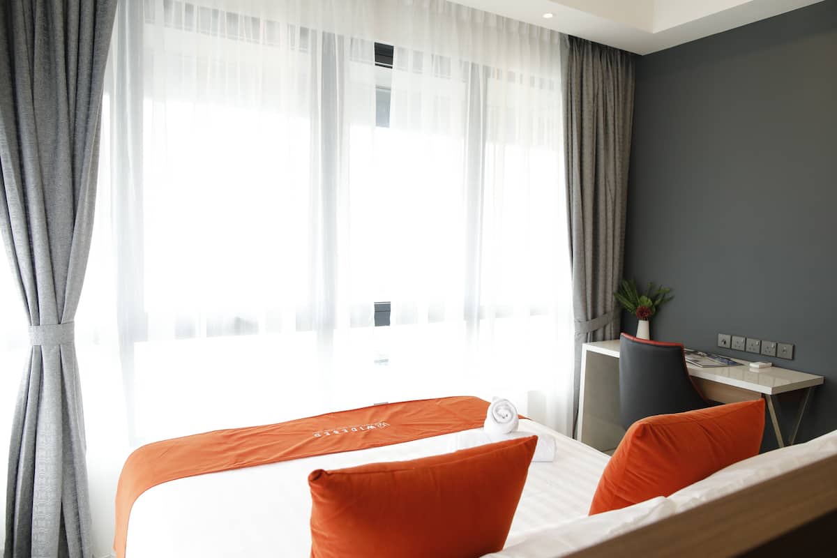 A hotel room with a bed, a desk, and a window with curtains.