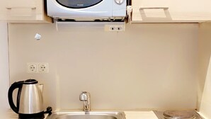 A compact kitchenette with a built-in microwave, a kettle, a sink, and a stove. - Innsbruck Apartment (Innsbruck)